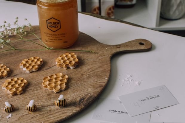 Aesthetic honey-themed composition with honeycomb shapes and jar of golden honey on wooden board.