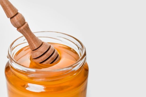 Glass jar of honey with a wooden dipper, set against a white background. Perfect for food and kitchen-related content.