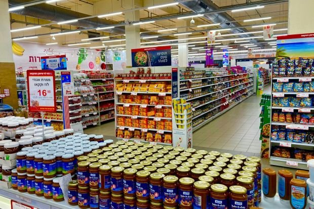 Wide view of a fully stocked supermarket aisle with jars and various products on shelves.
