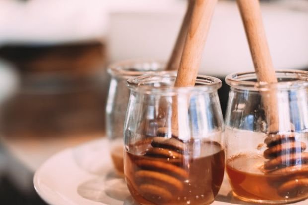 Three glass jars filled with honey and wooden dippers, elegantly displayed on a white plate.