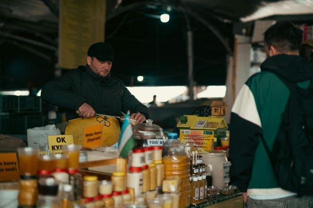 A vendor at an indoor market selling various honey jars. Captured in an atmospheric setting.